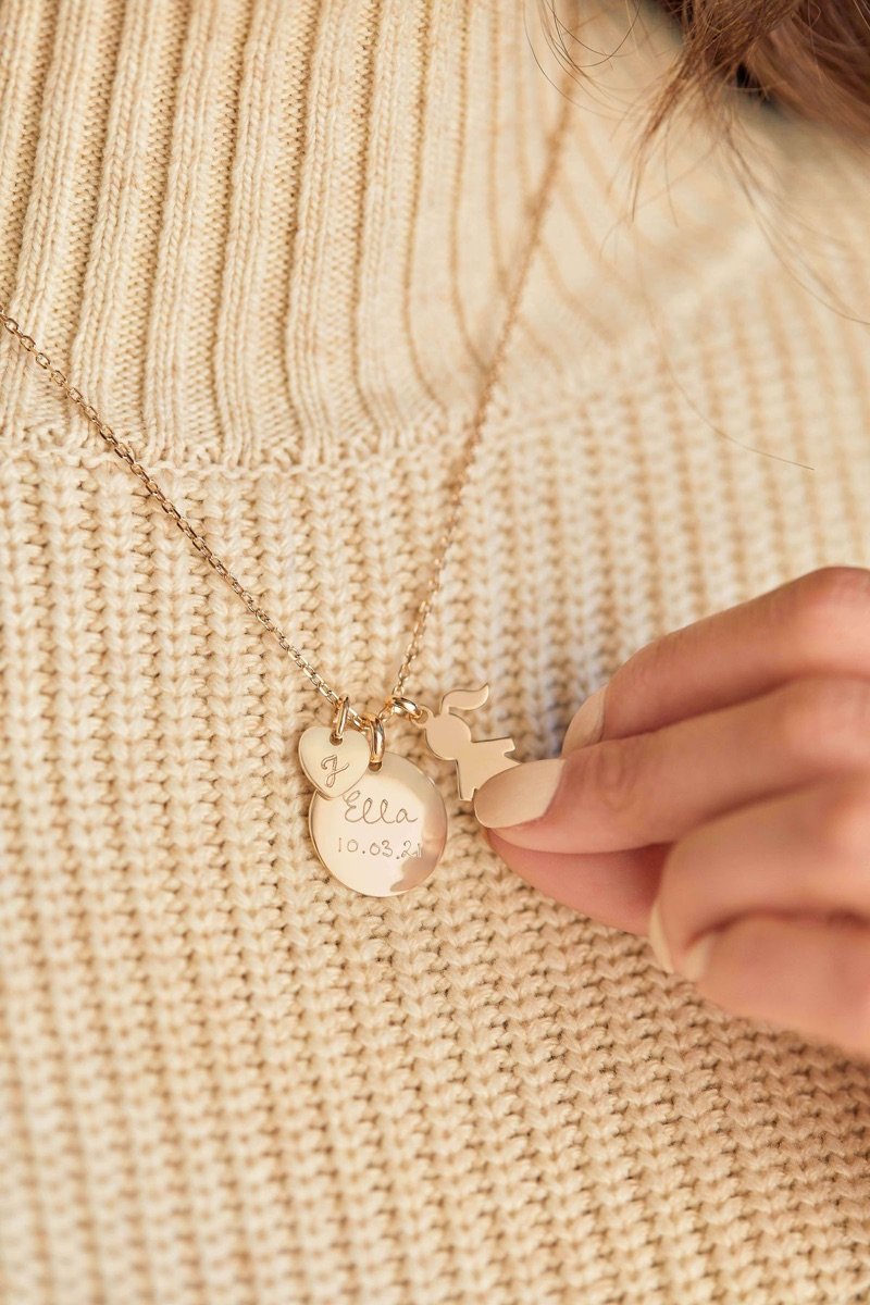 Collar dorado con medallas grabadas sobre un jersey de punto beige, campaña de rebajas de Hops